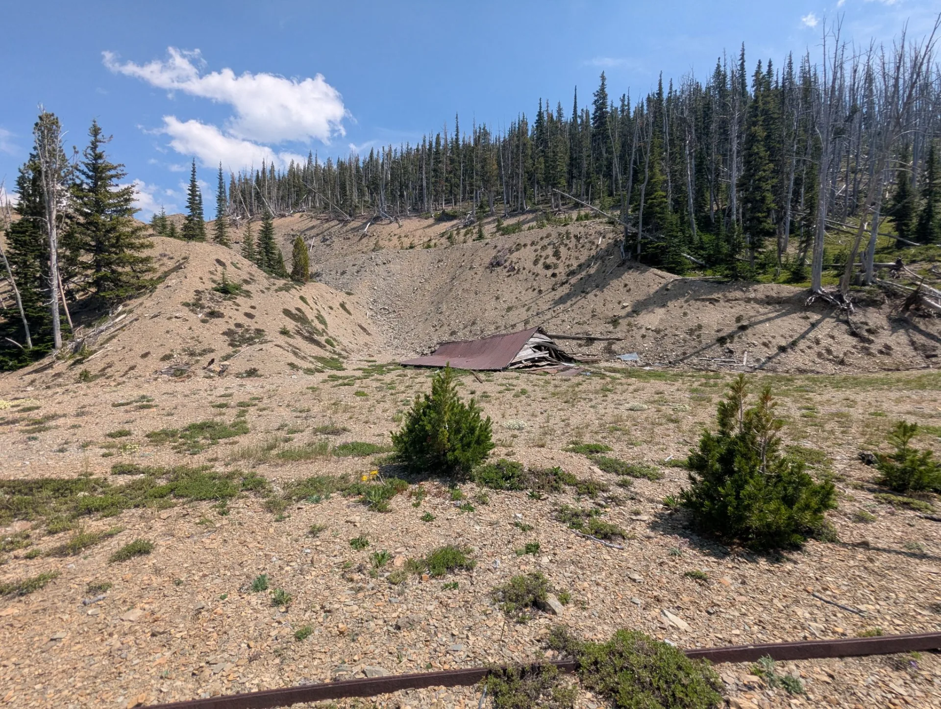 Historic open cut and waste rock dumps at the Cotter Basin workings, with a collapsed structure at the base of the cut.