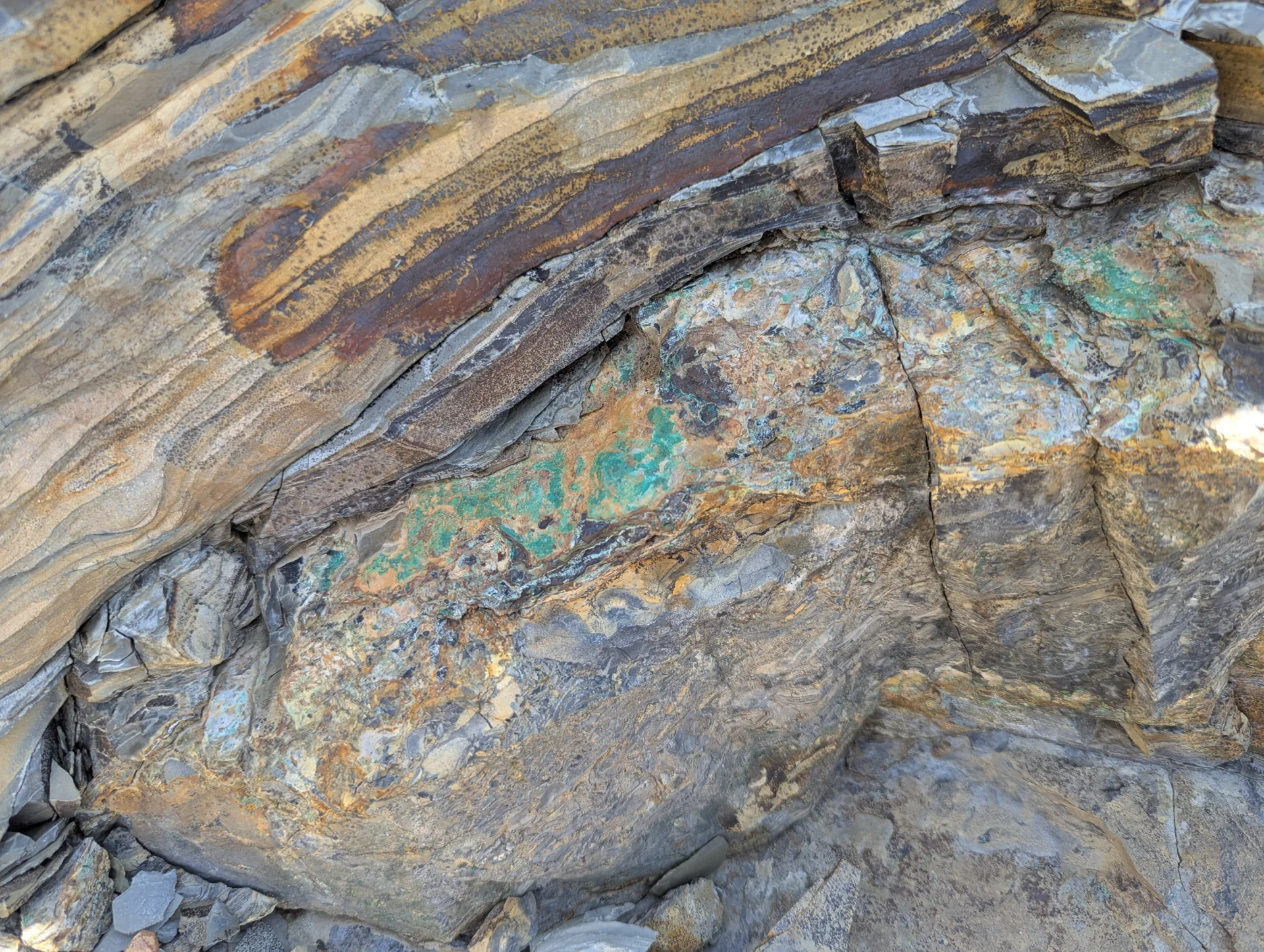 Copper oxides developed along bedding in the thin-bedded sedimentary host rock, exposed in outcrop.