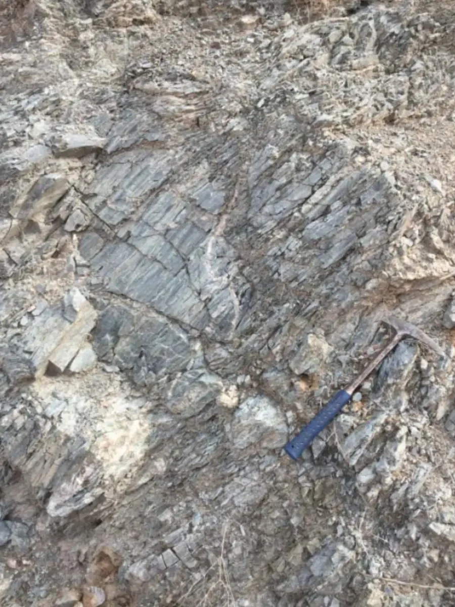 Foliated mica schist outcrop with hammer for scale