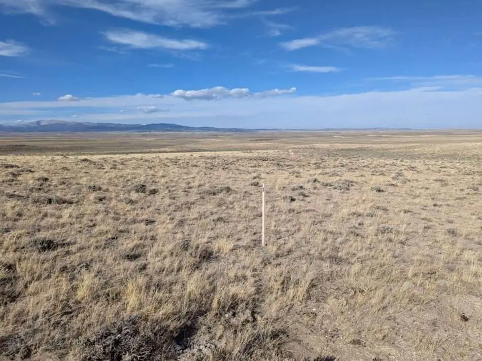 Expansive Wyoming high-desert plain with claim stake and distant mountains